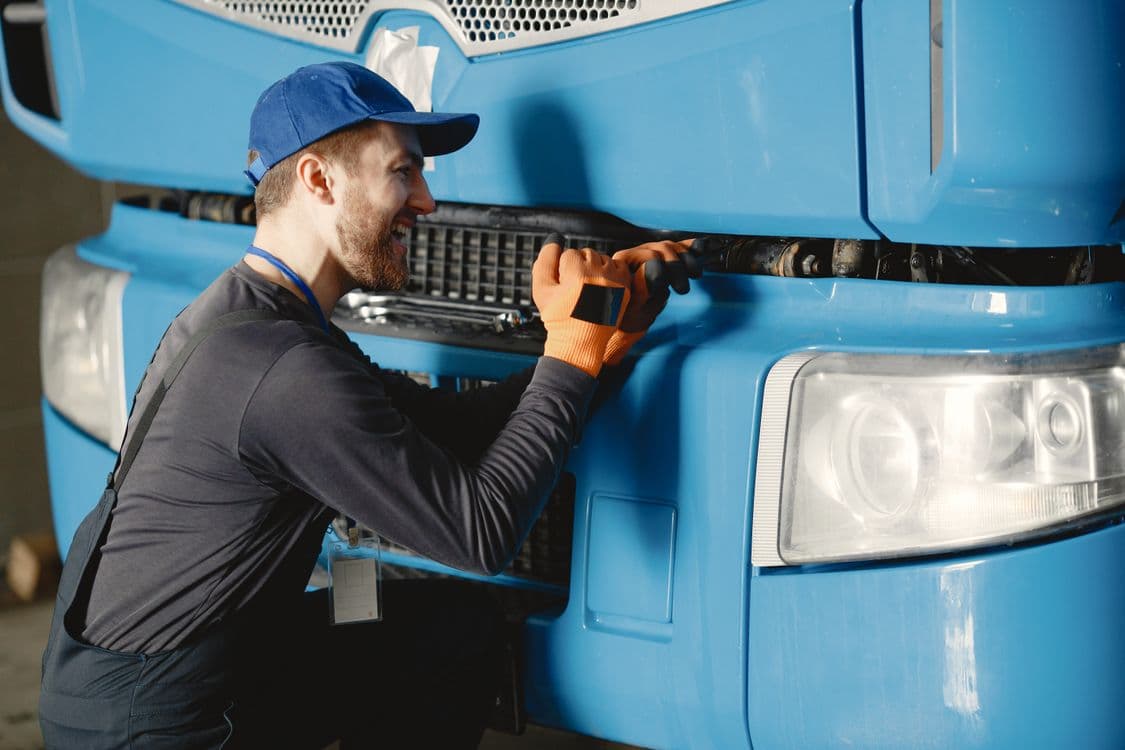 Mechanic inspecting a blue commercial truck in a service bay