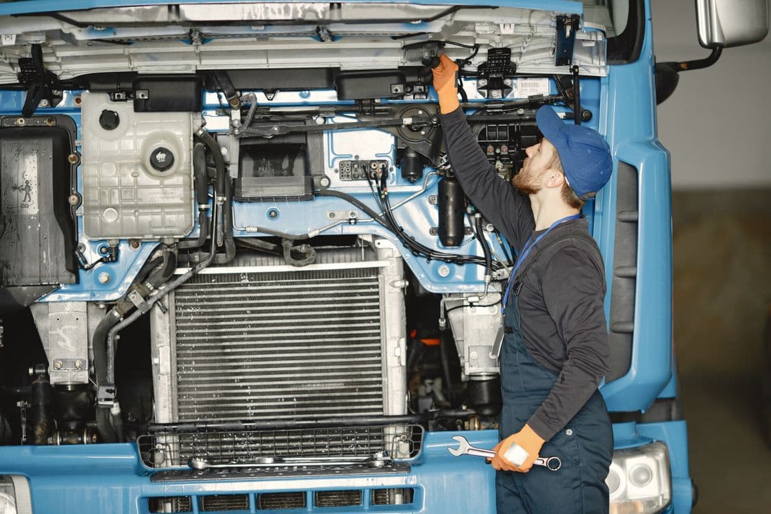 Mechanic checking the open engine bay of a blue commercial truck